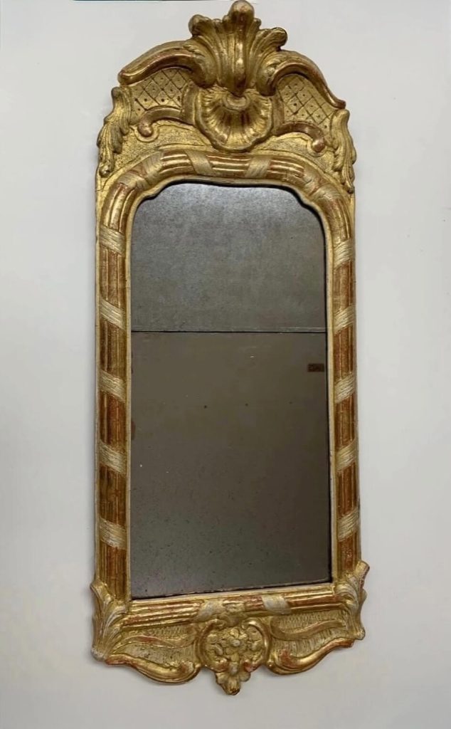 Antik förgylld spegel med dekorativ ram i rokoko med snidade ornament och smal spegelyta.